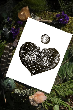 Pen & ink illustration of tree frogs gazing at the moon on a heart shaped lily pad. Gothic style art print by B. MacPherson Studio placed on moss and ferns.